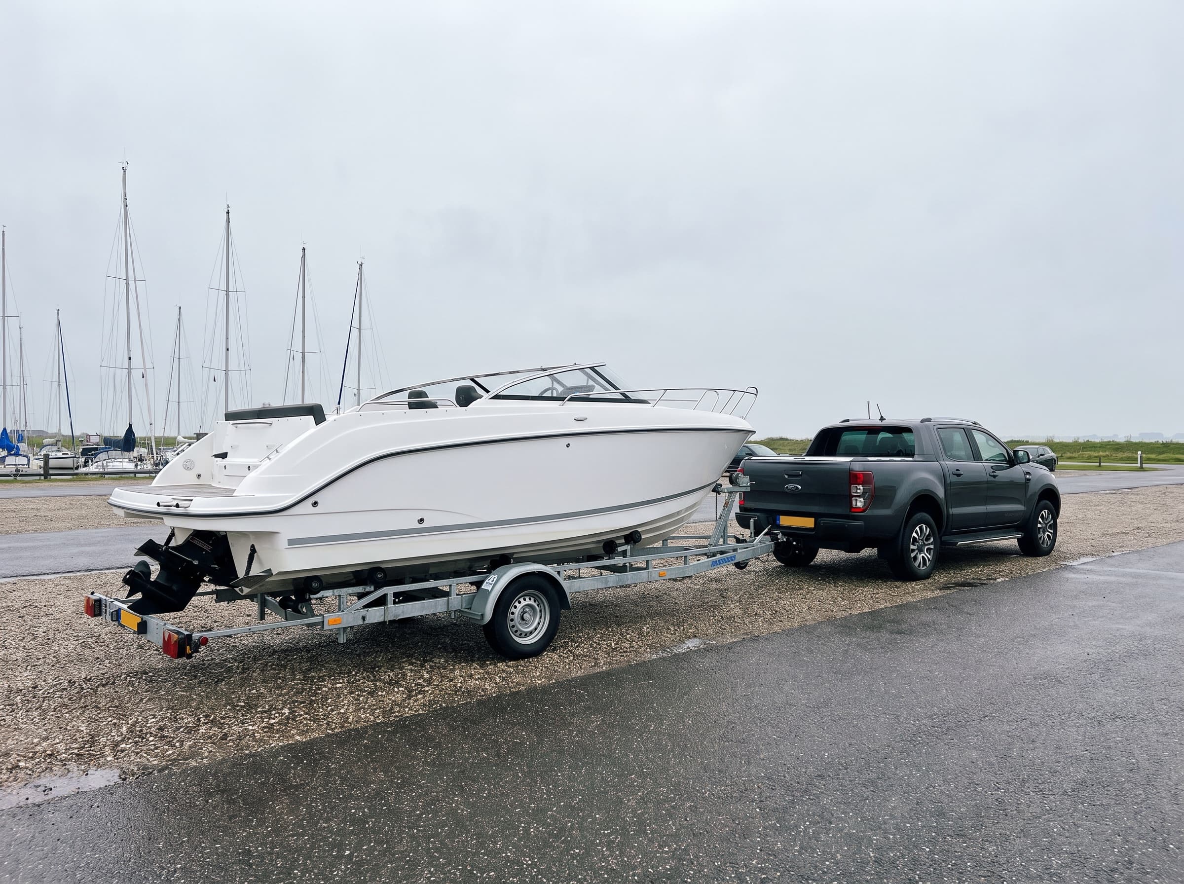 Speedboot op een boottrailer achter een pick-up bij een jachthaven