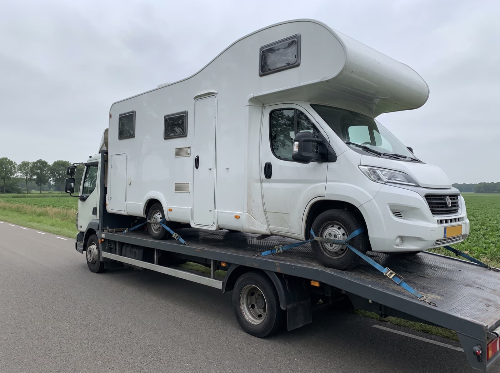 Alkoofcamper vastgezet op een vrachtwagen met laadvloer tijdens campertransport
