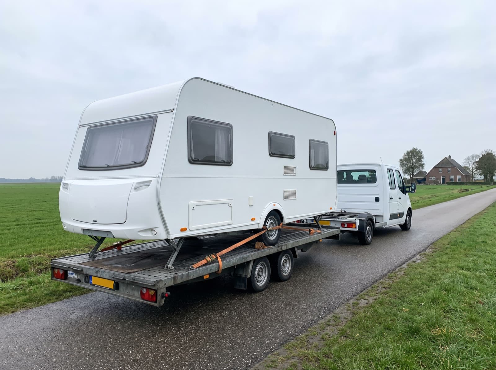 Caravan op een open trailer tijdens caravantransport over een polderweg